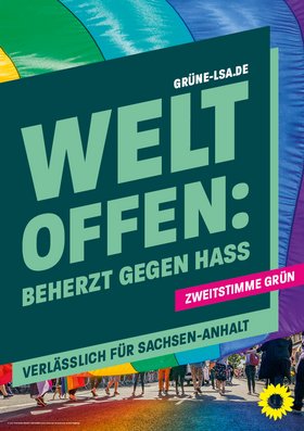 Vor einer großen regenbogenfarbenen Fahne steht das Banner mit der Aufschrift "Weltoffen: Beherzt gegen Hass – Verlässlich für Sachsen-Anhalt" und dem Hinweis "Zweitstimme Grün"